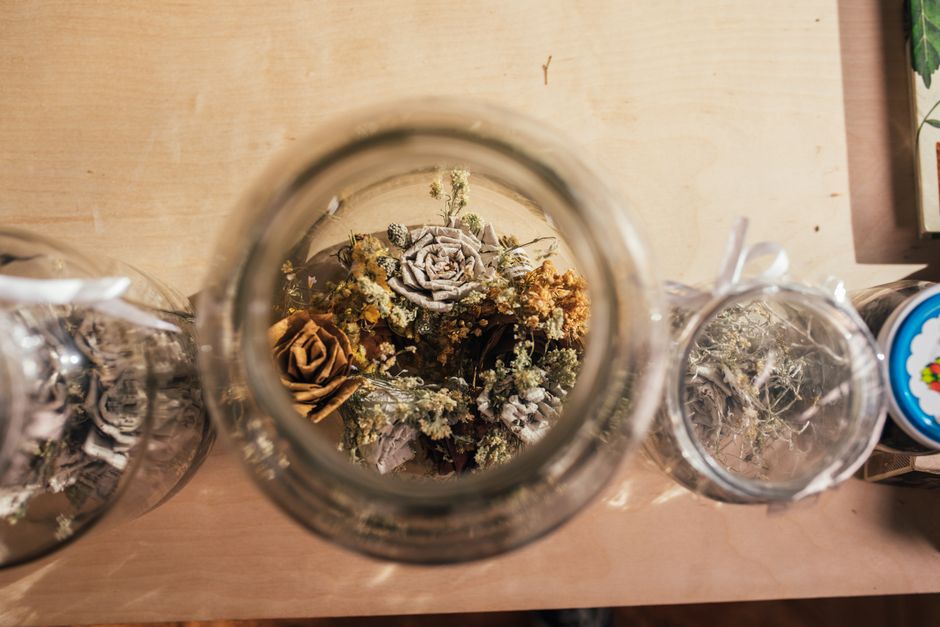 Aesthetic flat lay of dried flowers in glass jars on a wooden surface.
